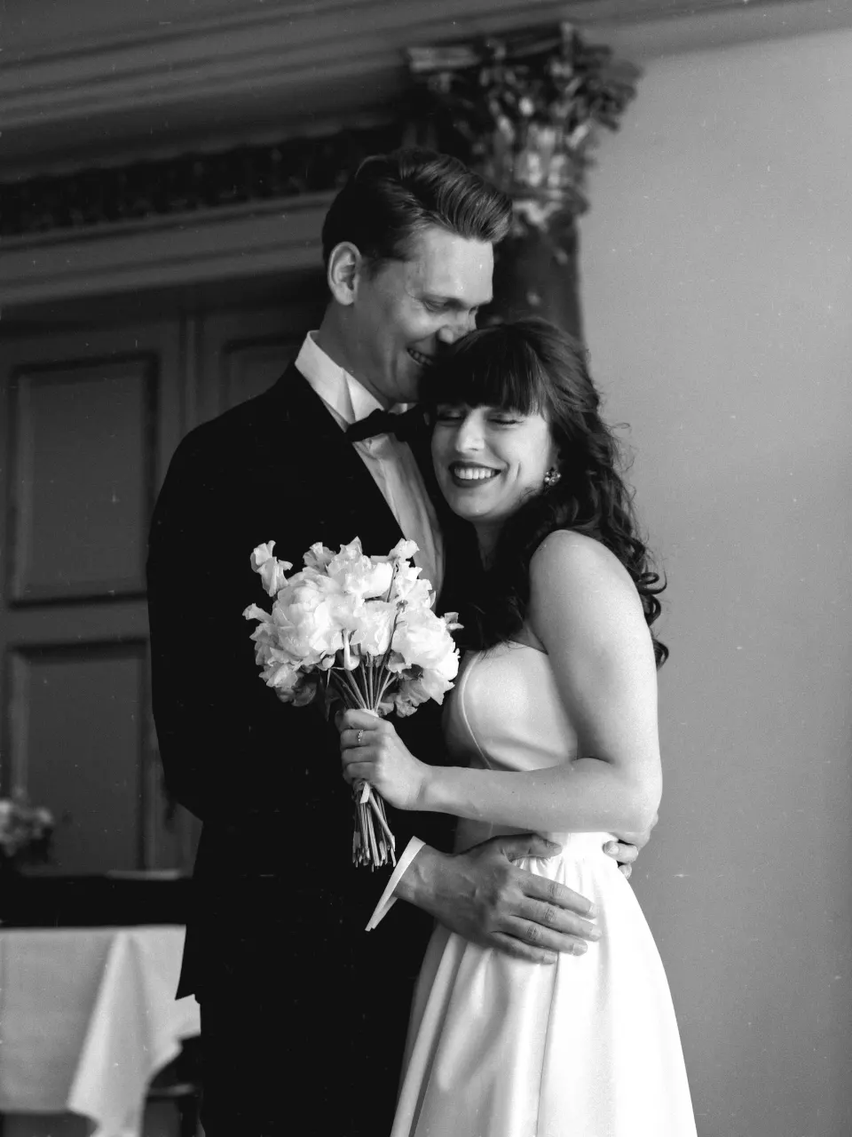 Groom embracing bride with bouquet, elegant black and white wedding portrait